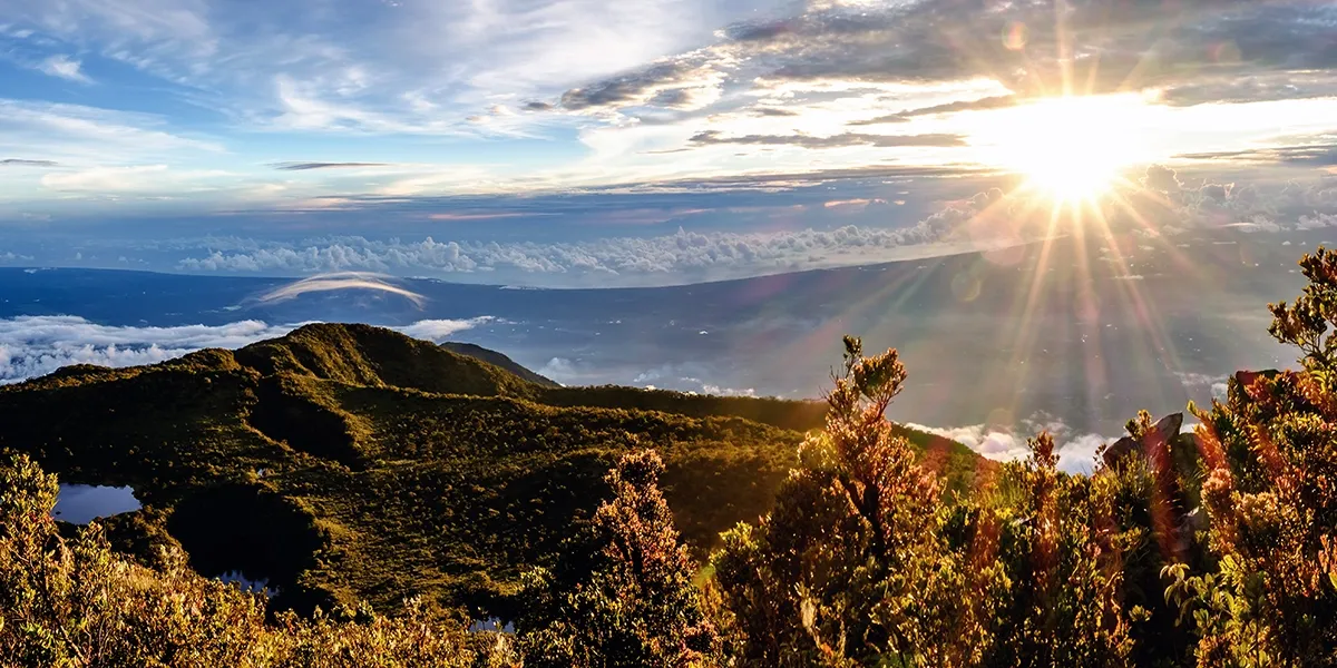 Sunrise breaking over forested ridges and a sea of cloud on the summit of Mt. Talamau